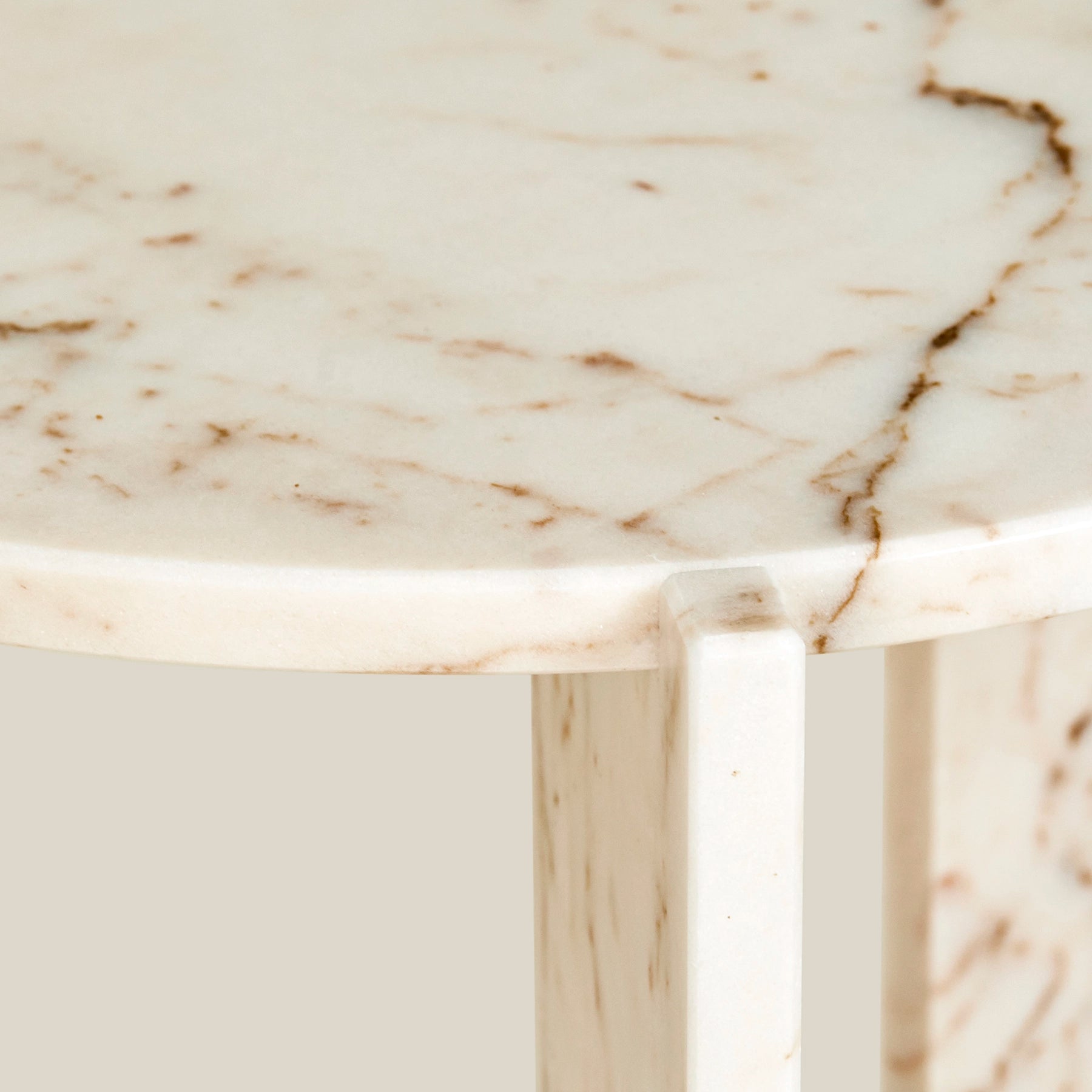 A close-up detail of a Minerva, a minimalistic, three-legged, round side table. Made from Rose Aurora marble.