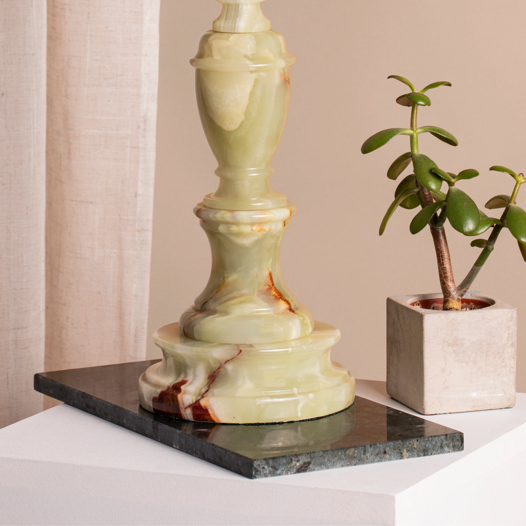 A close-up of vintage pale green onyx table lamp base on marble coaster and plinth.