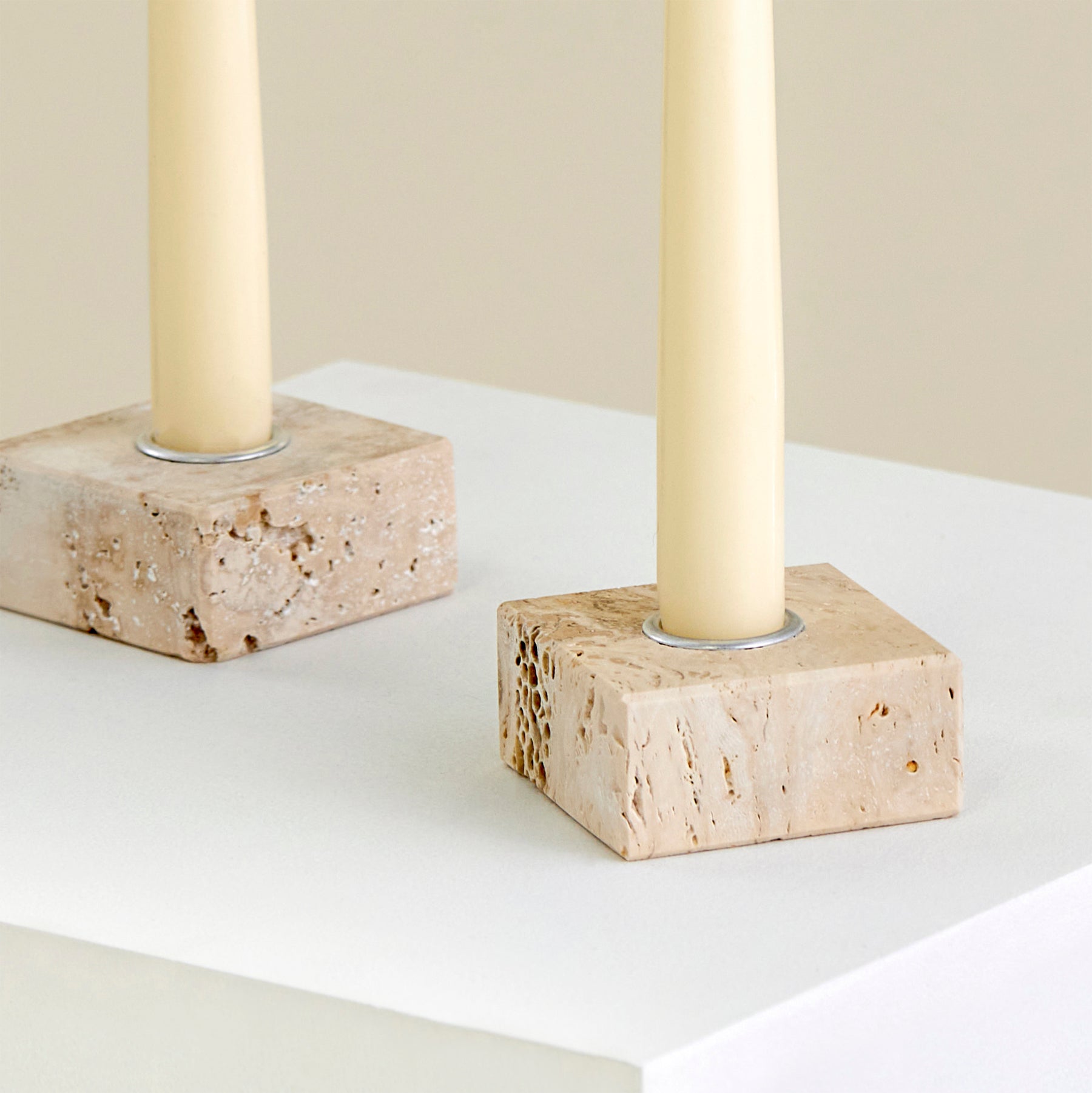 A close-up of two candle holders on a plinth made from Travertine marble with silver detailing.