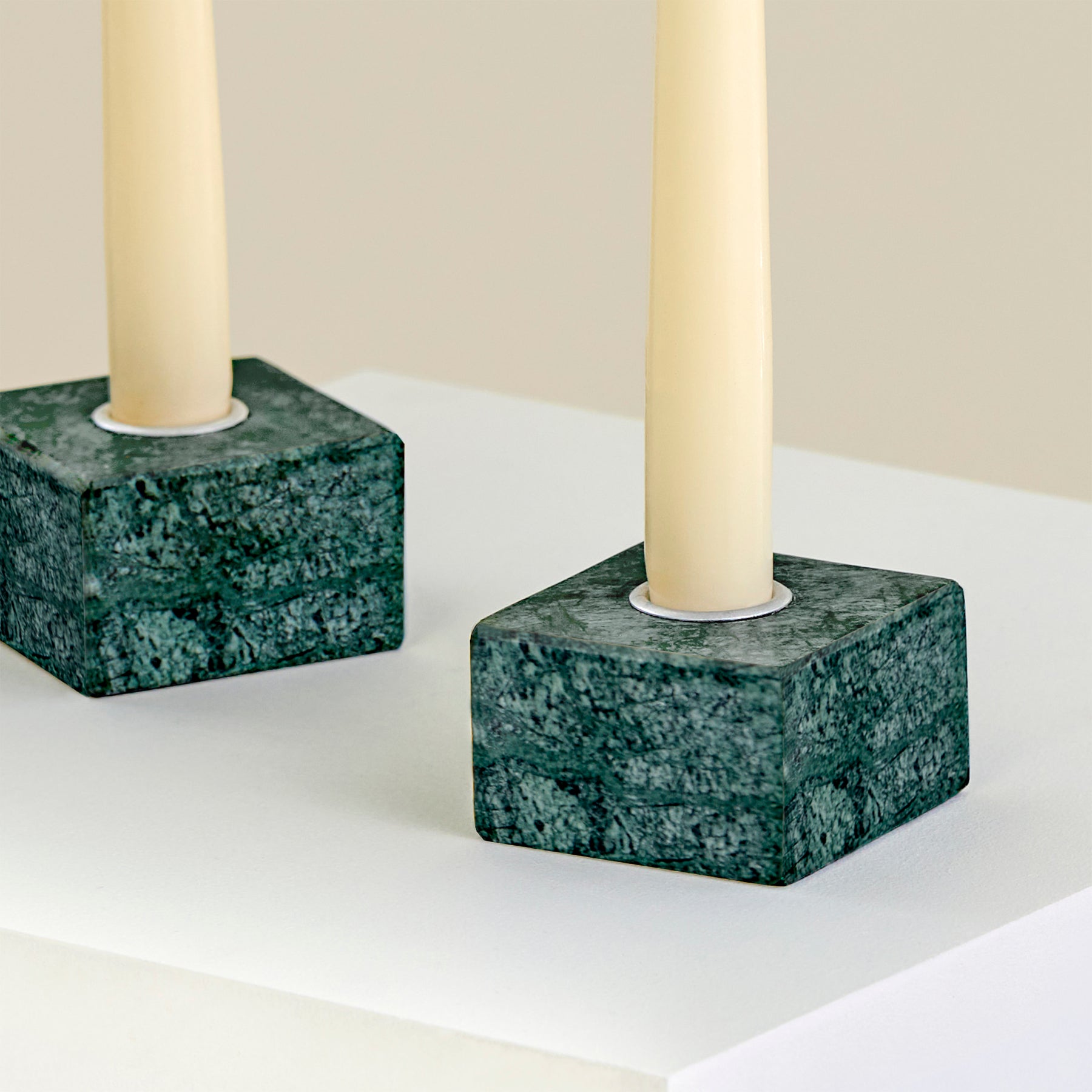 A close-up of two candle holders on a plinth made from Verde Guatemala marble with silver detailing.