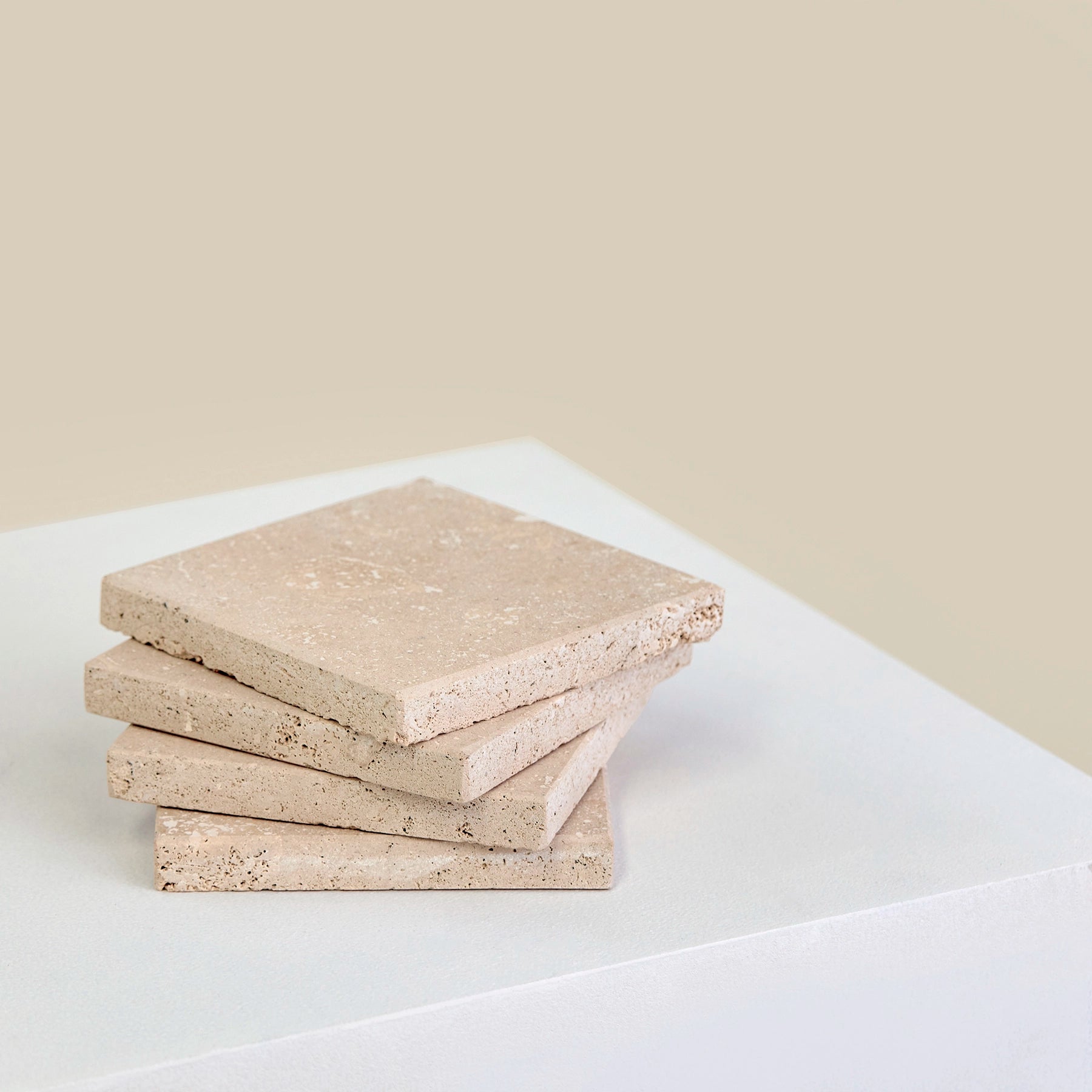 Four square, Travertine Romano marble coasters laid in a stack.