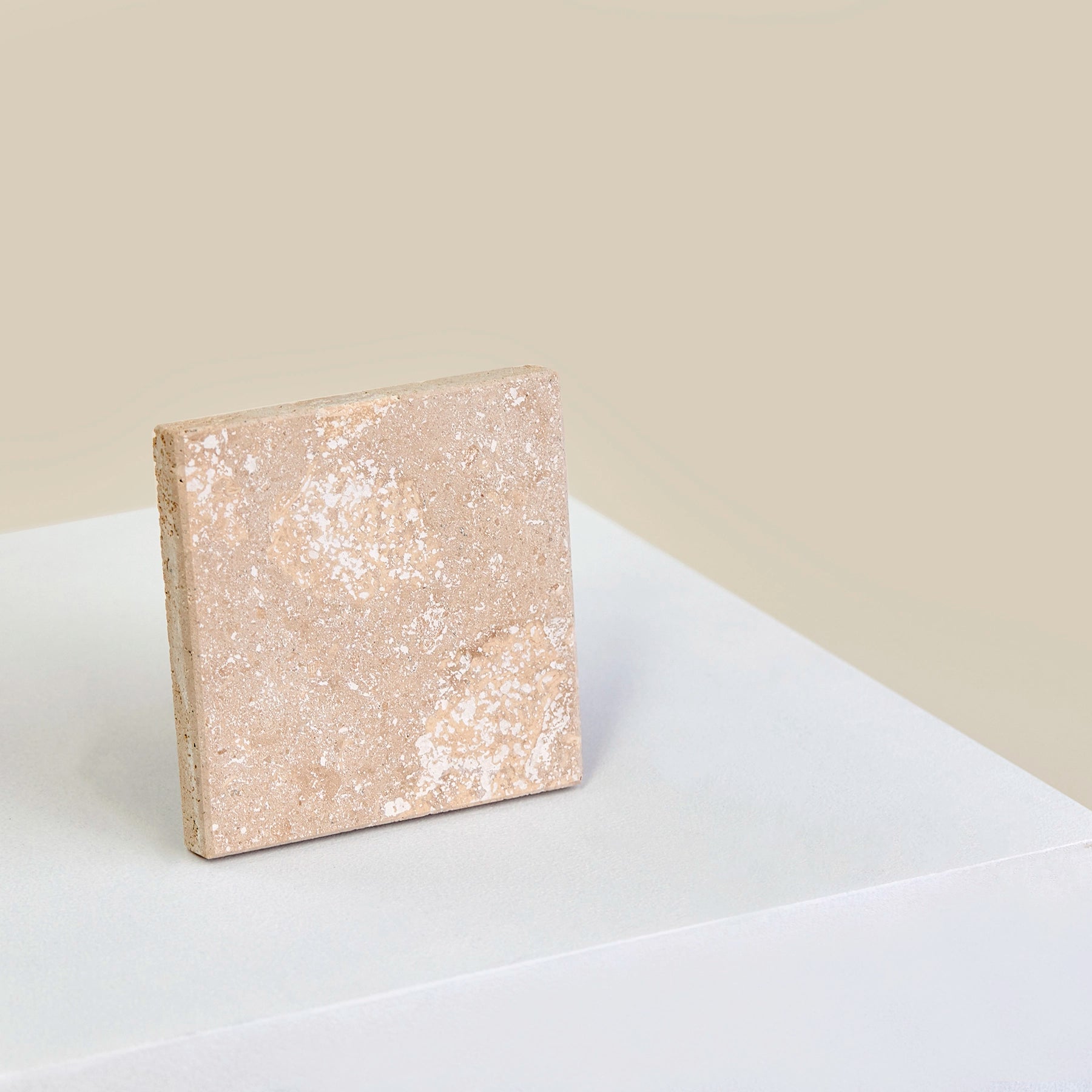 A square, Travertine Romano marble coaster stood up on its side.