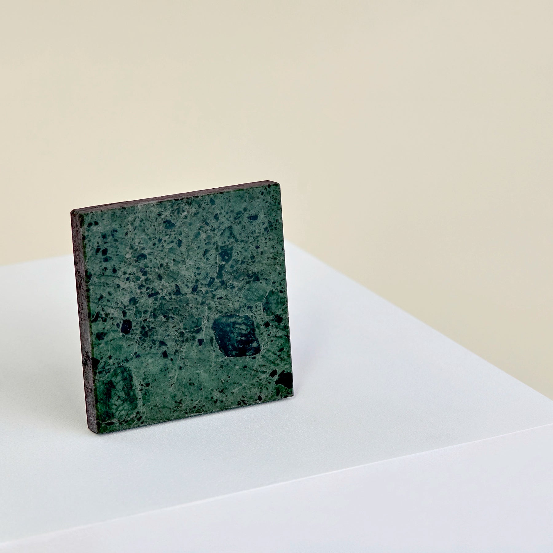 A square, verde guatemala marble coaster stood up on its side.