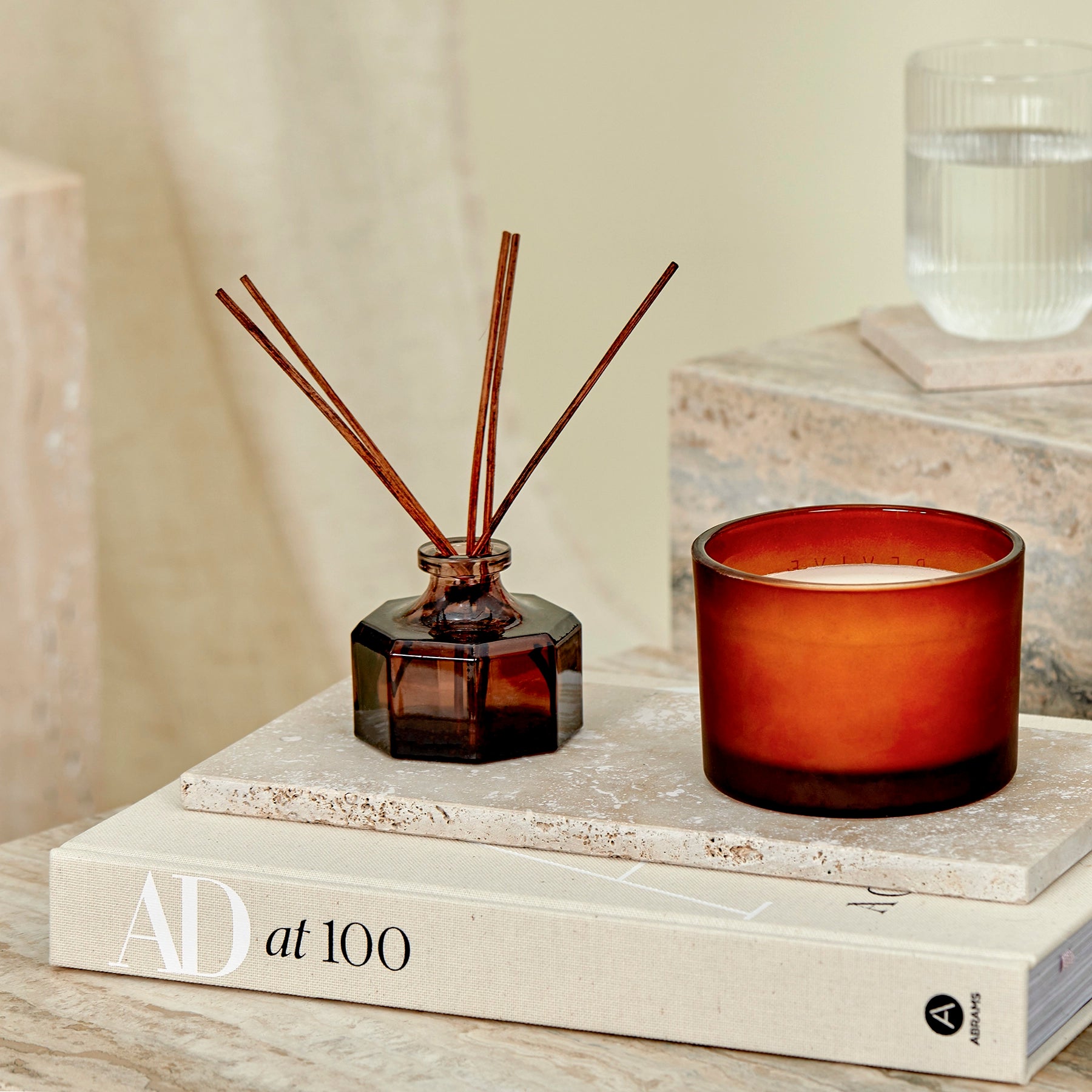 A close-up of a glass diffuser and candle on a travertine marble tray and side tables.