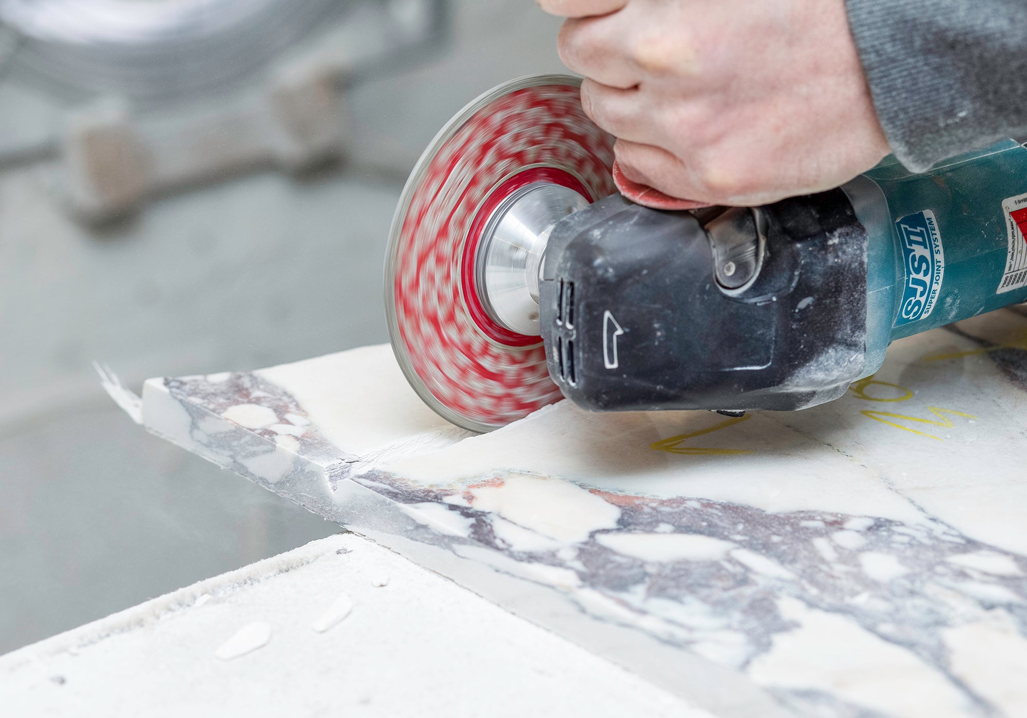 A close-up of a hand holding a circular saw, hand crafting marble furniture in the Marmo Lusso workshop.